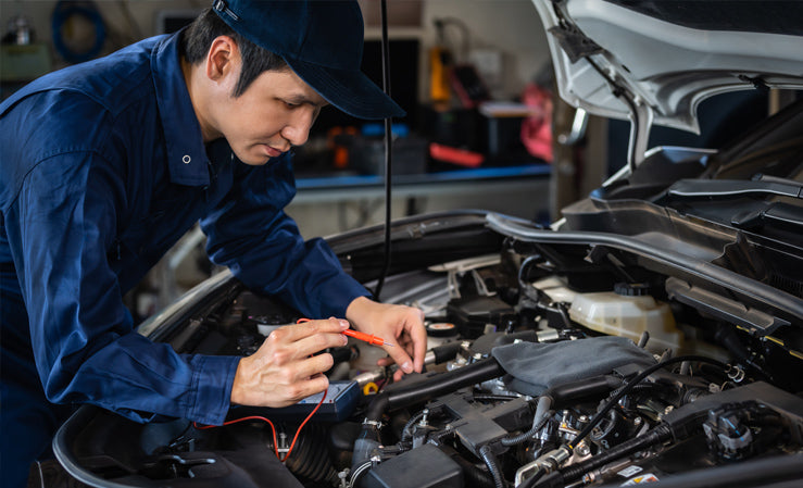 Technician using clamp multimeter to troubleshoot auto electrical issues